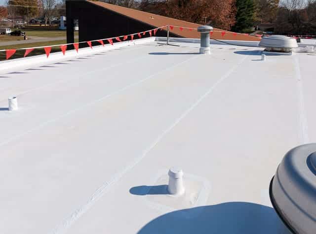 Bright white silicone coated flat roof secured with safety flags along the perimeter