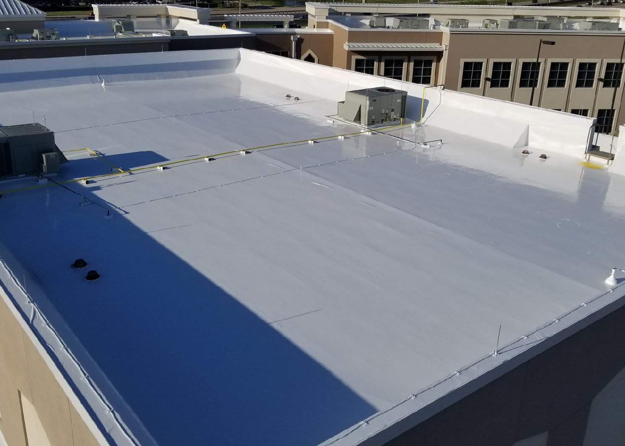 Large commercial flat roof coated in bright white silicone, viewed from an adjacent building