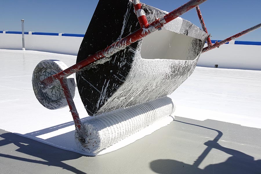 Silicone roof coating being applied with a roller on a bright sunny day